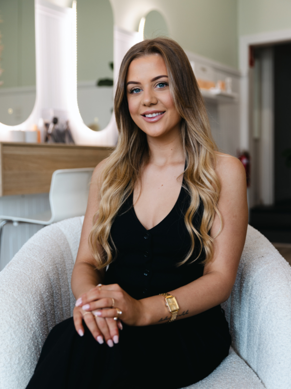 Emily Whiteway, owner of Makeup & Beauty Lounge in Moonee Ponds, sitting in a chair smiling for a professional headshot, representing expert beauty services, lash and brow treatments, and makeup application.