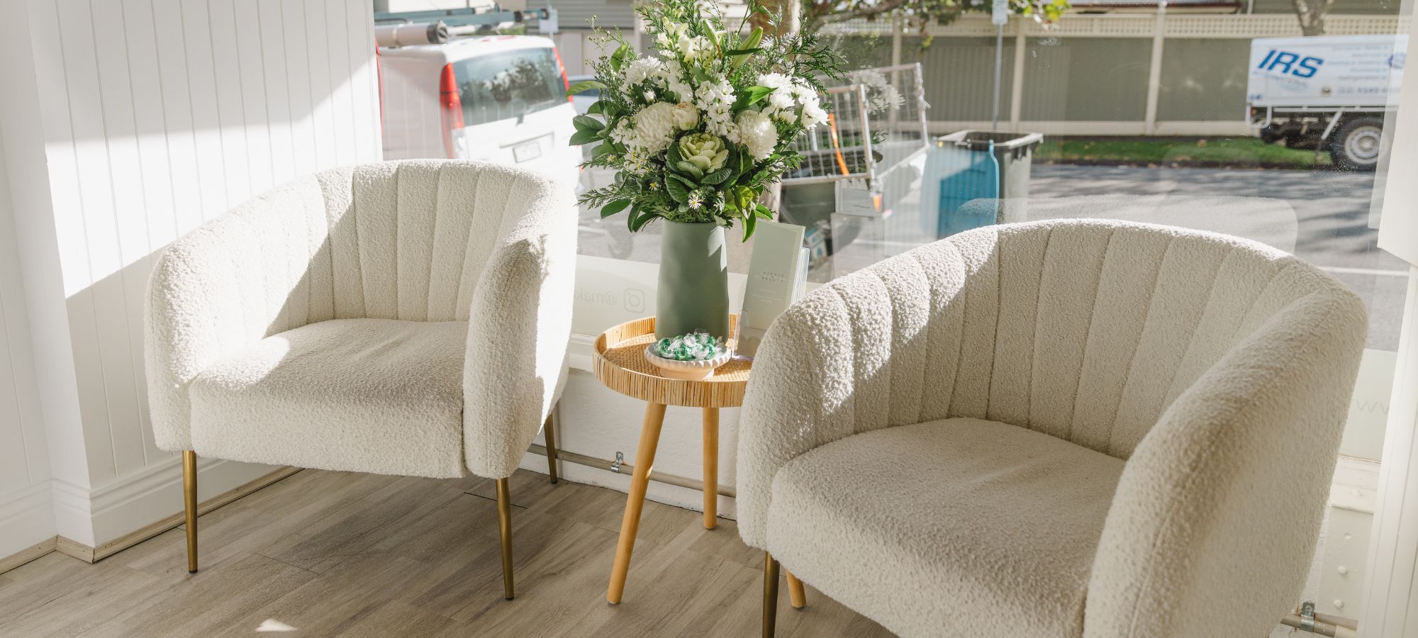 Salon seating area at Makeup & Beauty Lounge Moonee Ponds featuring stylish white chairs and a beautiful floral arrangement, creating a welcoming space for clients enjoying lash extensions, brow treatments, spray tans, waxing, and body sculpting services