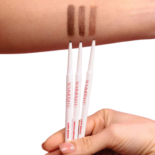 Summer and Lu brow pencils in dark, medium, and light brown shades with swatches on forearm showing creamy, smudge-proof texture for natural, defined brows.