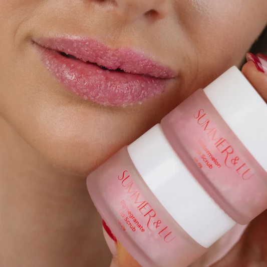 Close-up of lips with exfoliating pomegranate lip scrub applied, holding two jars of Summer & Lu Pomegranate Lip Scrub product.