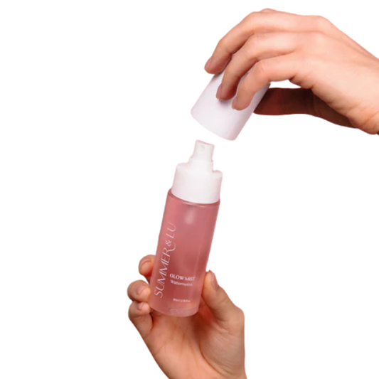 Hand holding Summer & Lu Watermelon Glow Mist bottle with white cap being removed, pink hydrating facial mist spray bottle.